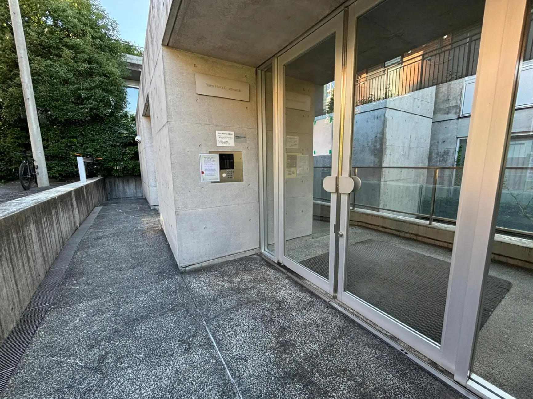 現代的な建物のエントランス、透明なガラスドア、コンクリートの外壁、掲示板、自転車が見える外観