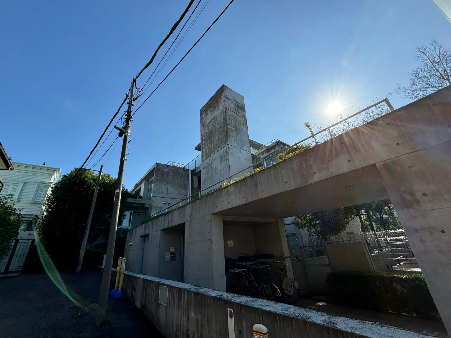日差しが輝く都市のコンクリート造りの建物と駐輪スペース、電線と木々が映る風景