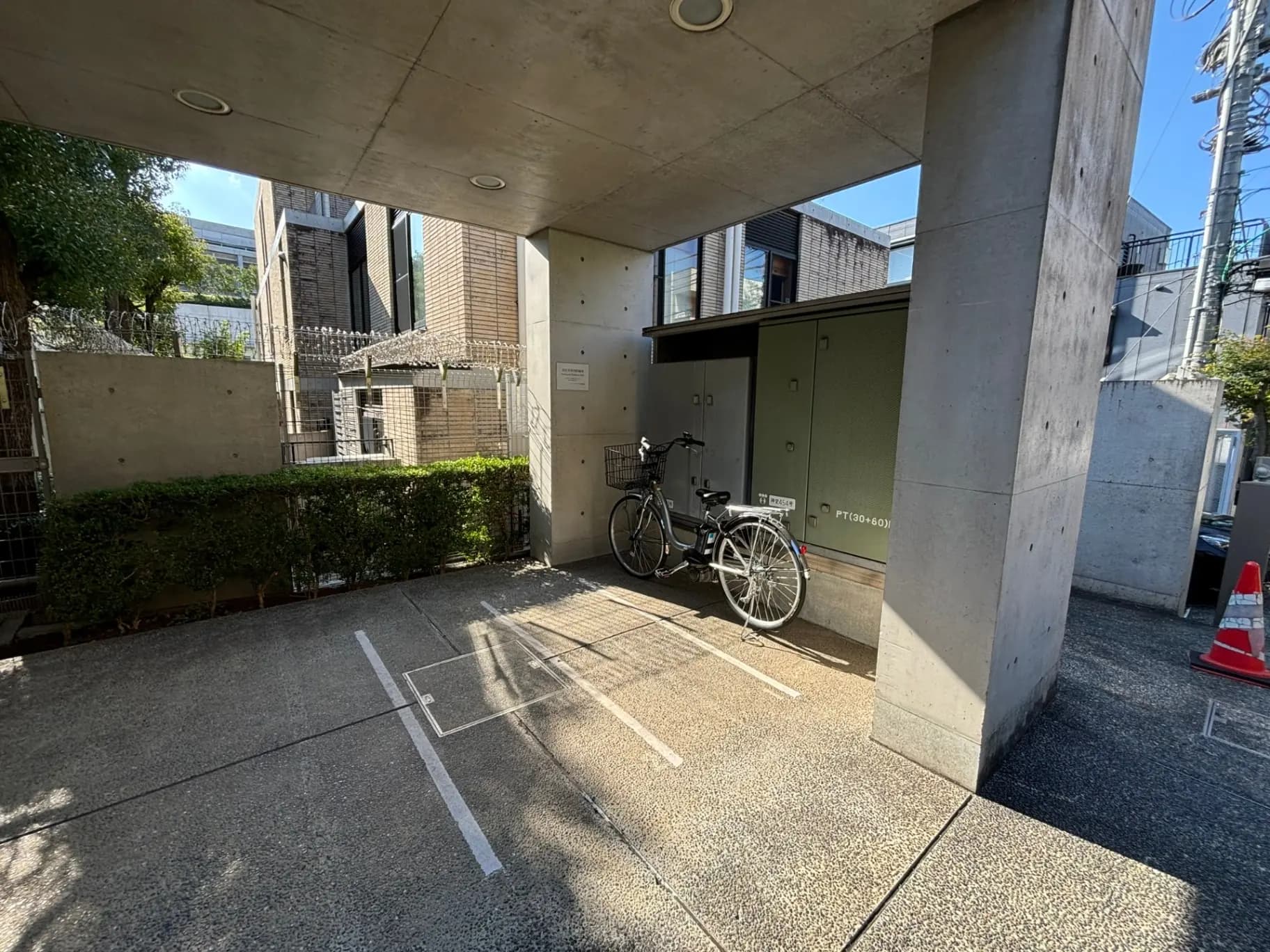 日差しが差し込むモダンなマンションの駐輪場、コンクリート柱とグリーンの植栽