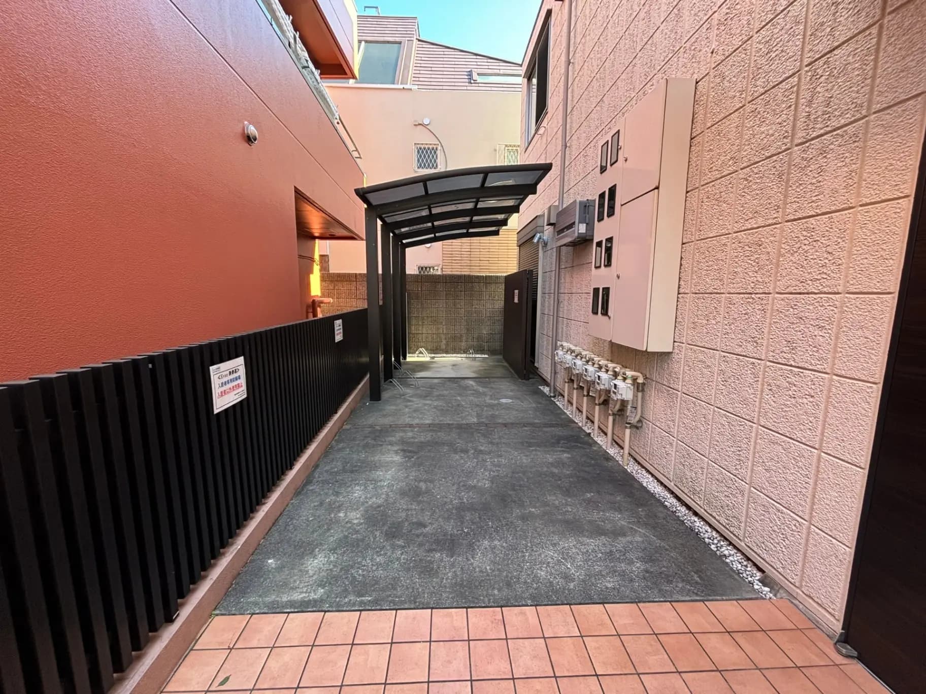 都会の建物の間にある狭い通路、赤茶色の壁と黒いフェンスが特徴的な都市風景