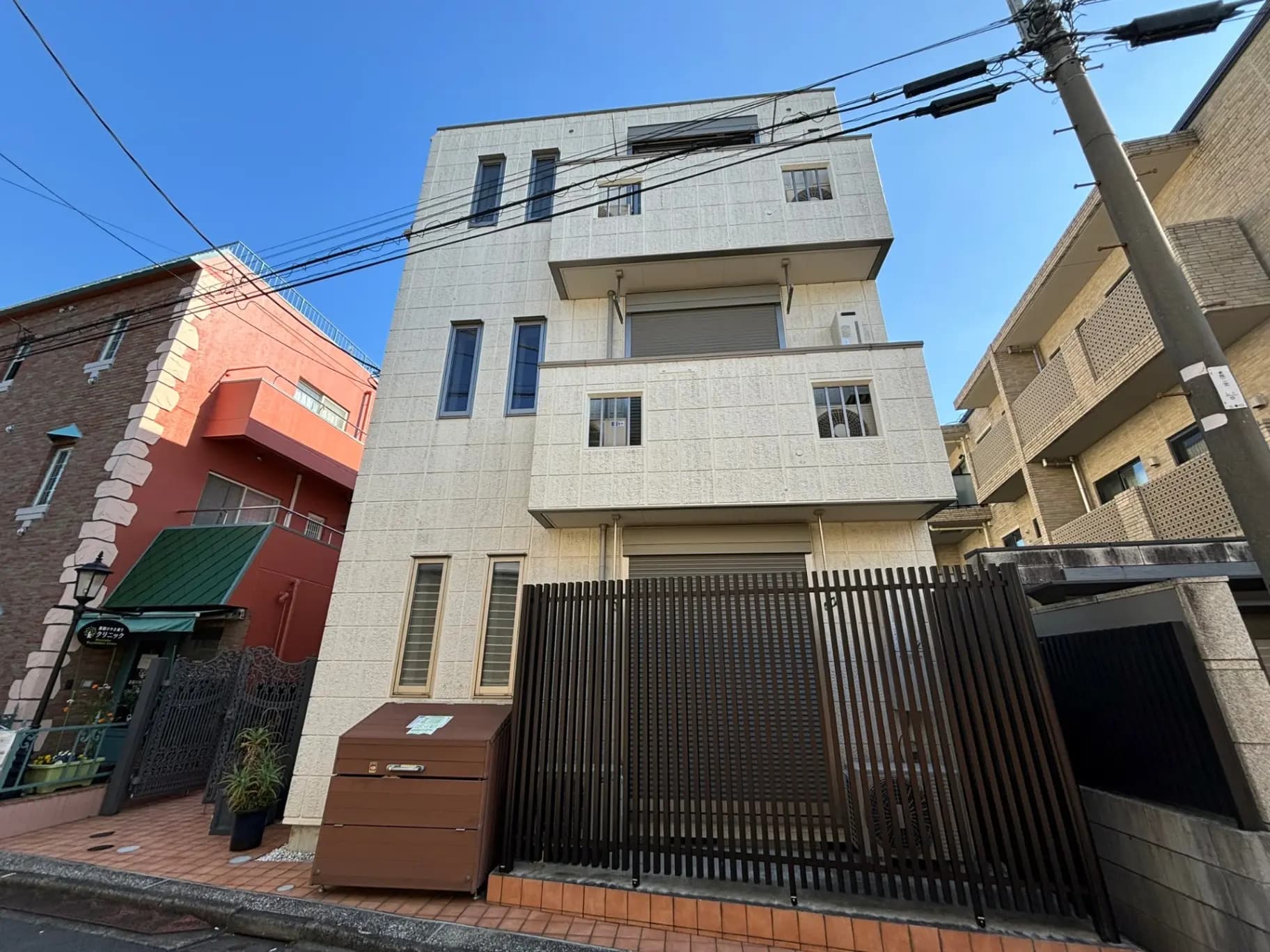 日差しが明るく照らす住宅街の風景、現代的な建築様式の建物と路地、電線が交差する空の一部