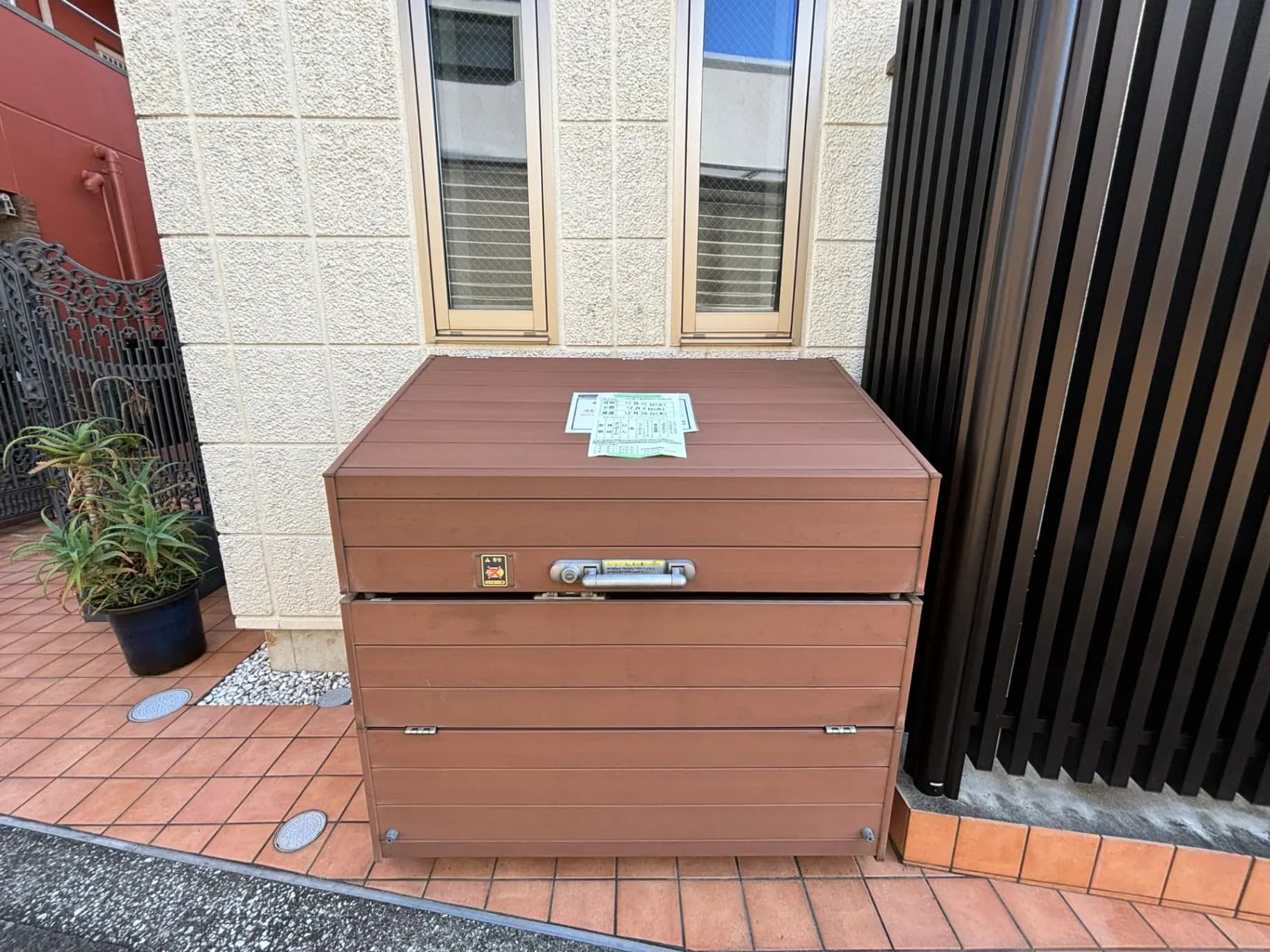 戸建て住宅のエントランスに設置された茶色の宅配ボックス、新聞が上に置かれている外観