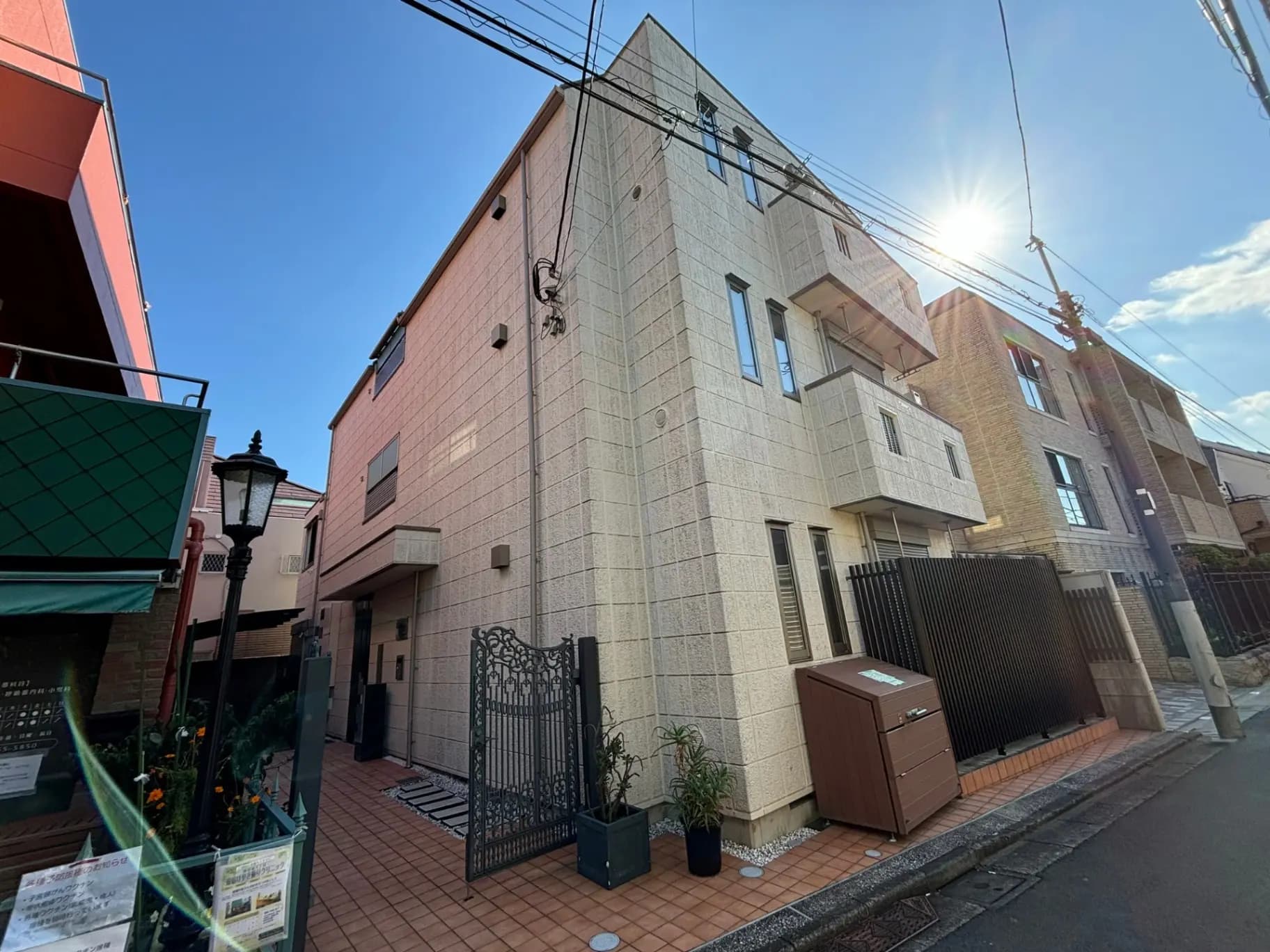 日差しが眩しい青空の下、都市の住宅街に建つモダンなアパートメントビルの外観