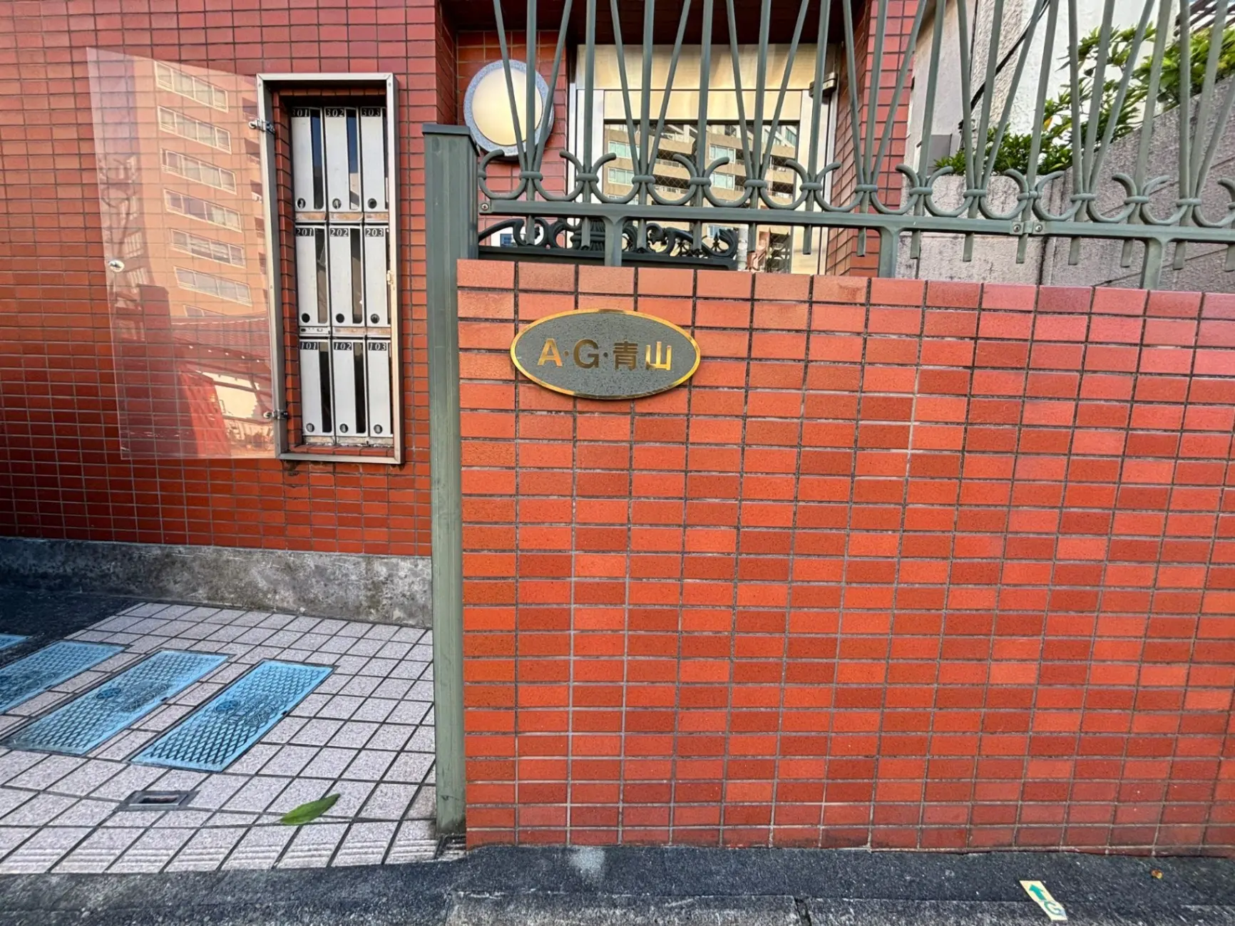赤レンガ造りの外壁に取り付けられた金属製の表札とデザイン性のある門扉、都市の歩道