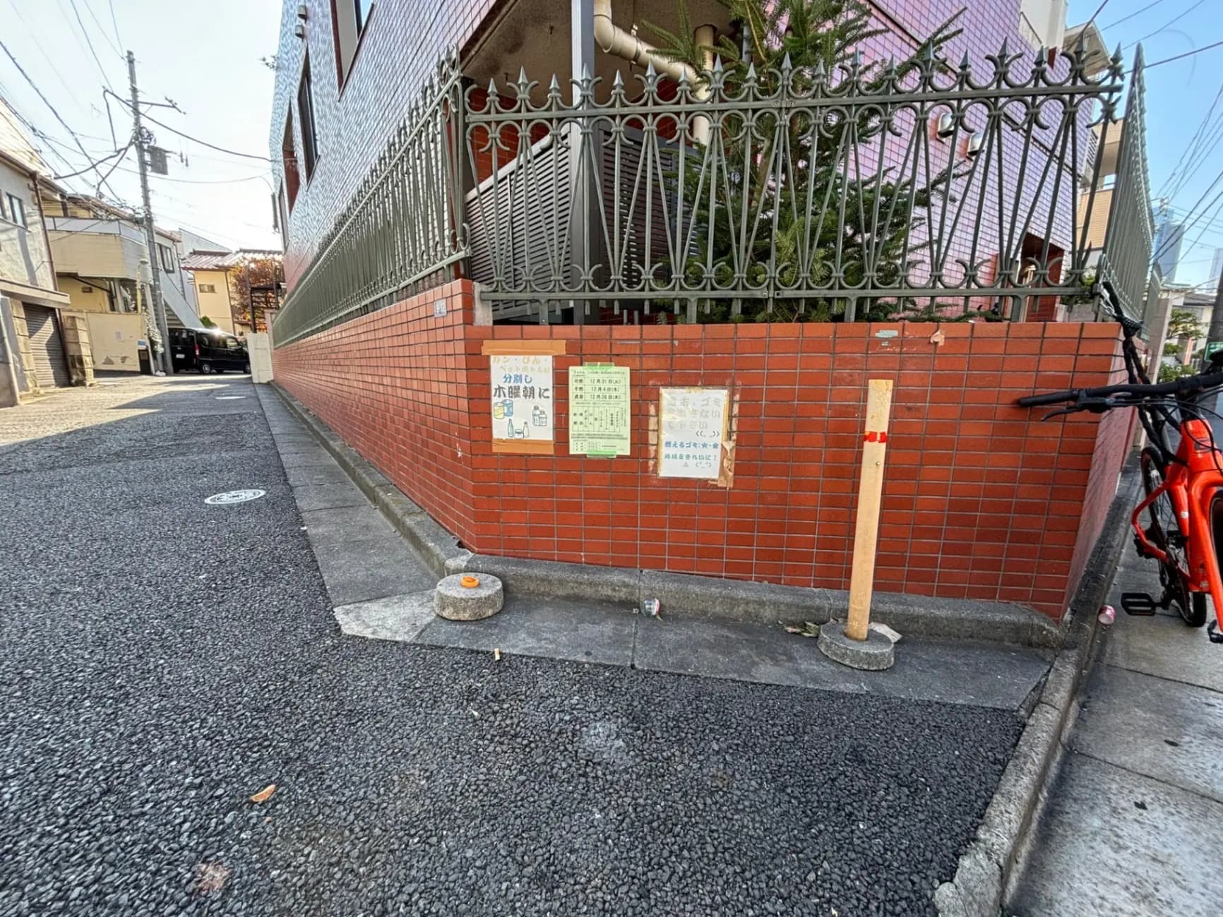 日本の住宅街の角、レンガ造りのフェンスと駐輪スペース、注意書きの看板が掲げられた歩道