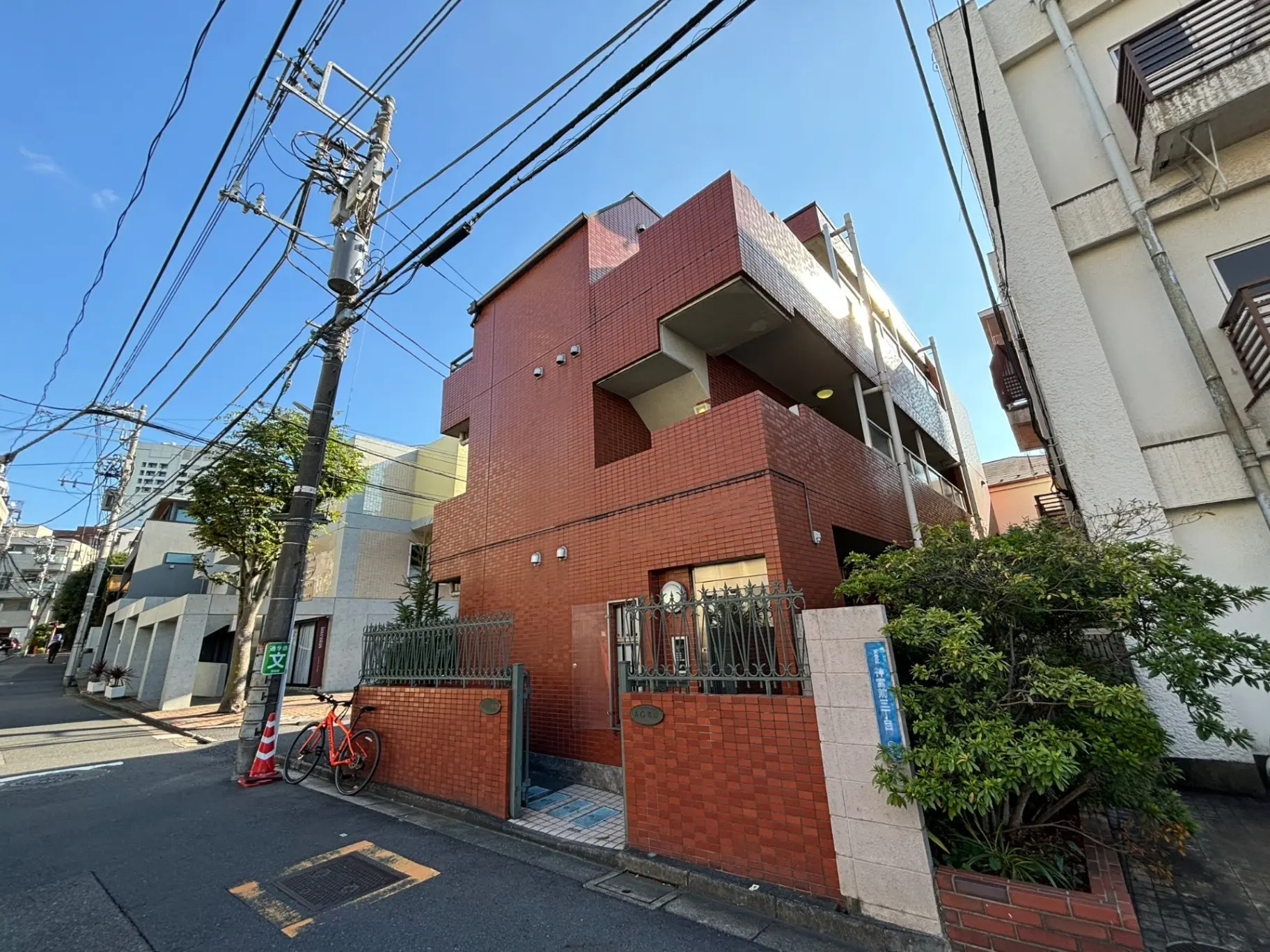 都市の住宅街にある赤レンガ造りのモダンなアパートメント、青空と電信柱、自転車が駐輪された歩道