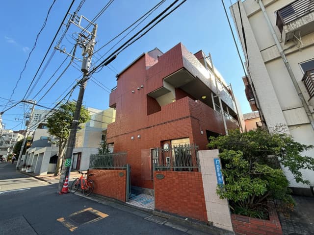 都市の住宅街にある赤レンガ造りのモダンなアパートメント、青空と電信柱、自転車が駐輪された歩道