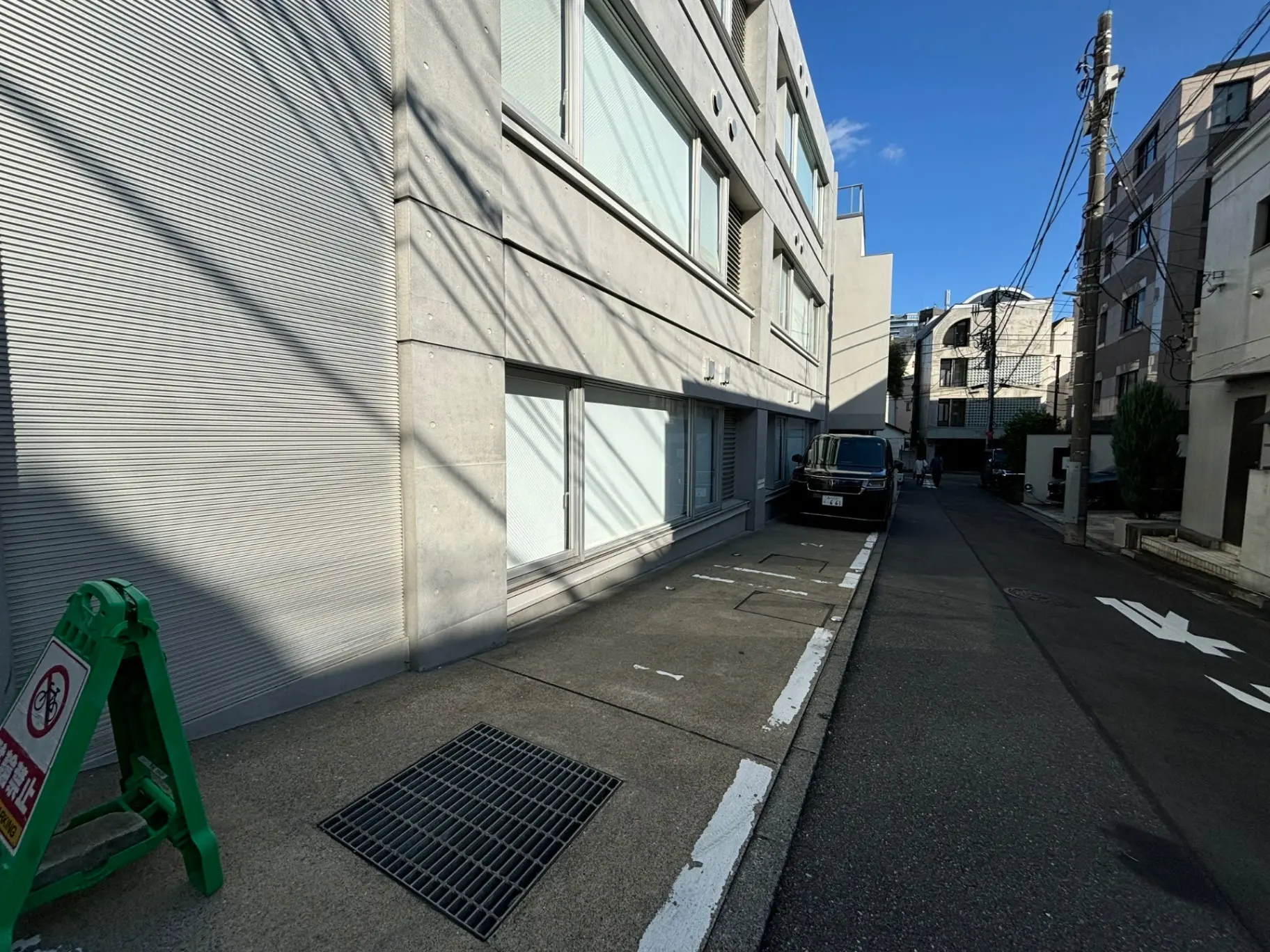 日差しが差し込む都市の小道と現代的な建物のファサード、歩行者と駐車している車