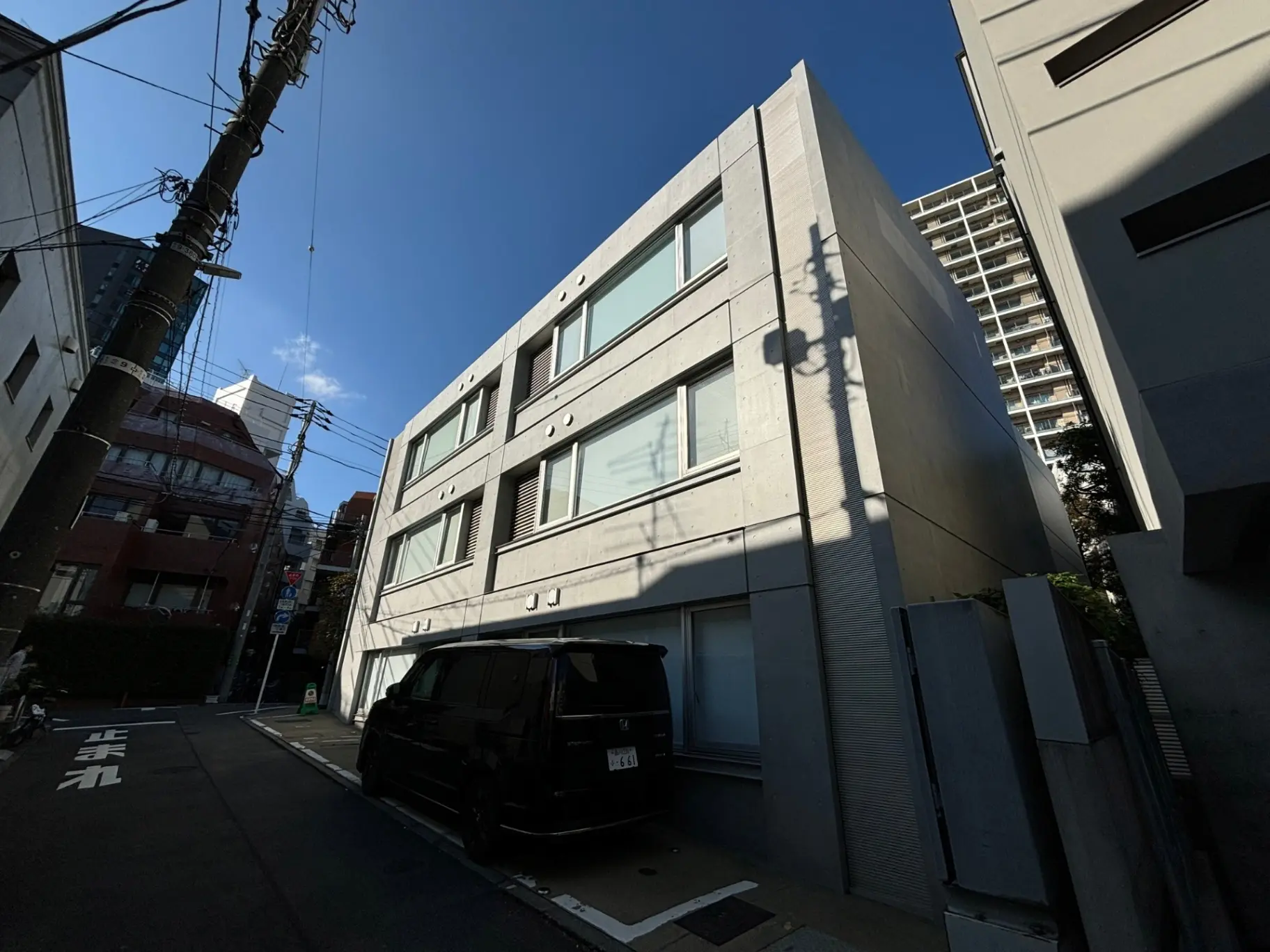 現代的な外観の都市型住居、日本の閑静な住宅街に建つコンクリート打ちっぱなしの建物と駐車された黒い車