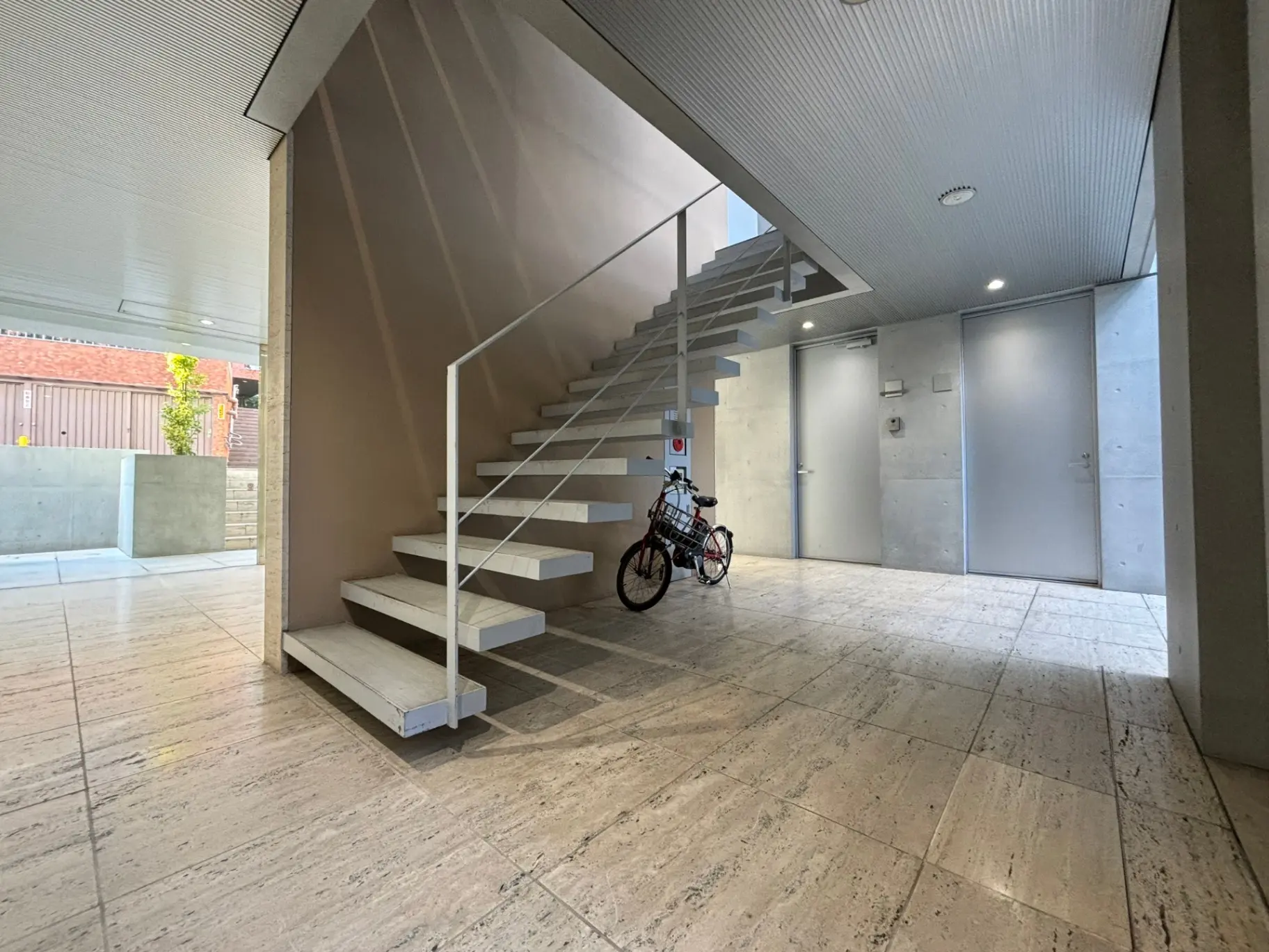 モダンな建築スタイルのエントランスホール、白い階段、コンクリートの壁、自転車が置かれた清潔感のある空間