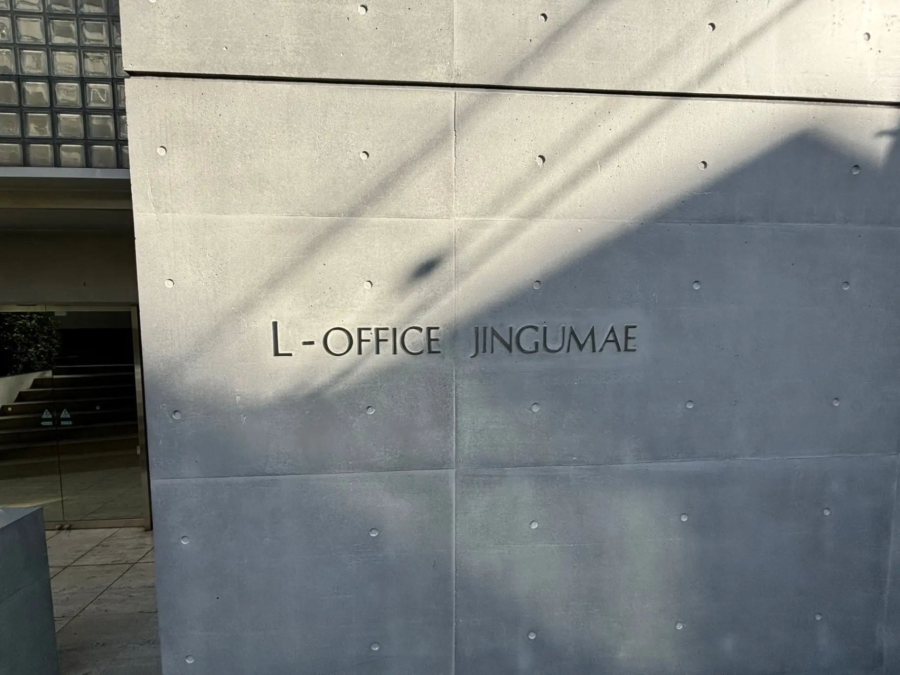 コンクリート壁に影が落ちるL-OFFICE JINGUMAEのロゴサイン