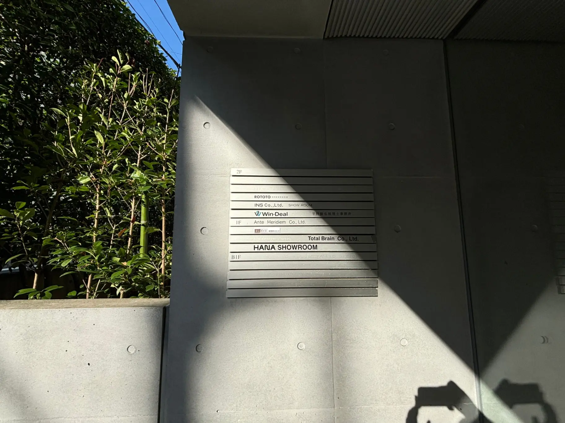 日差しの中で建物の外壁に設置された案内板、樹木と影が映る都市風景