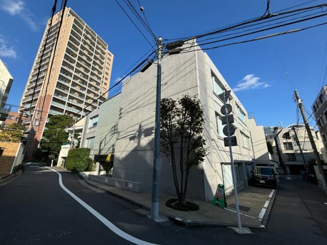 晴れた日の都会の住宅街、曲がり角にあるモダンな建物と高層マンション、電線と青空