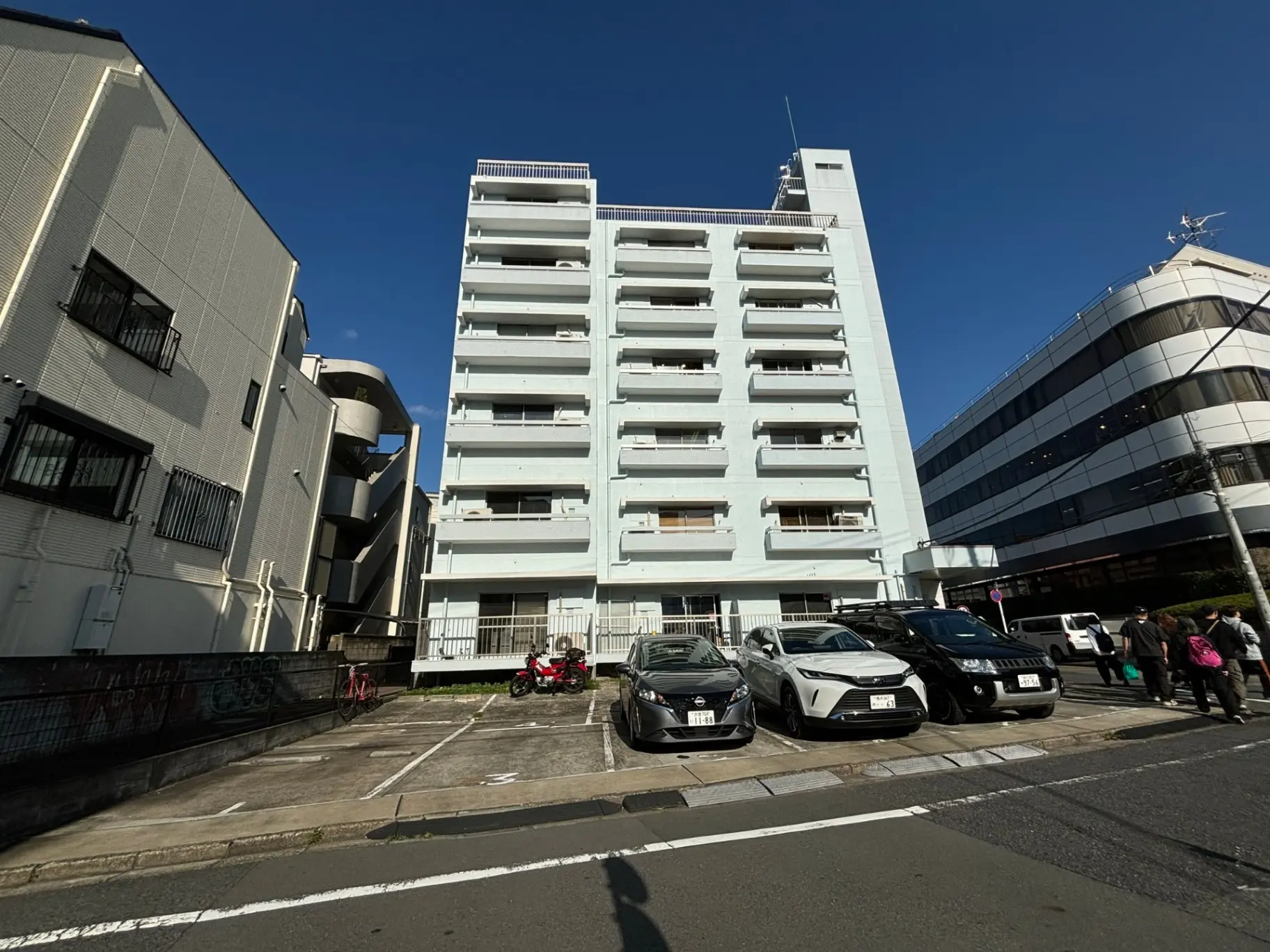 晴れた日の都市風景、白いマンションと近代的なオフィスビル、駐車場に停められた車と歩行者