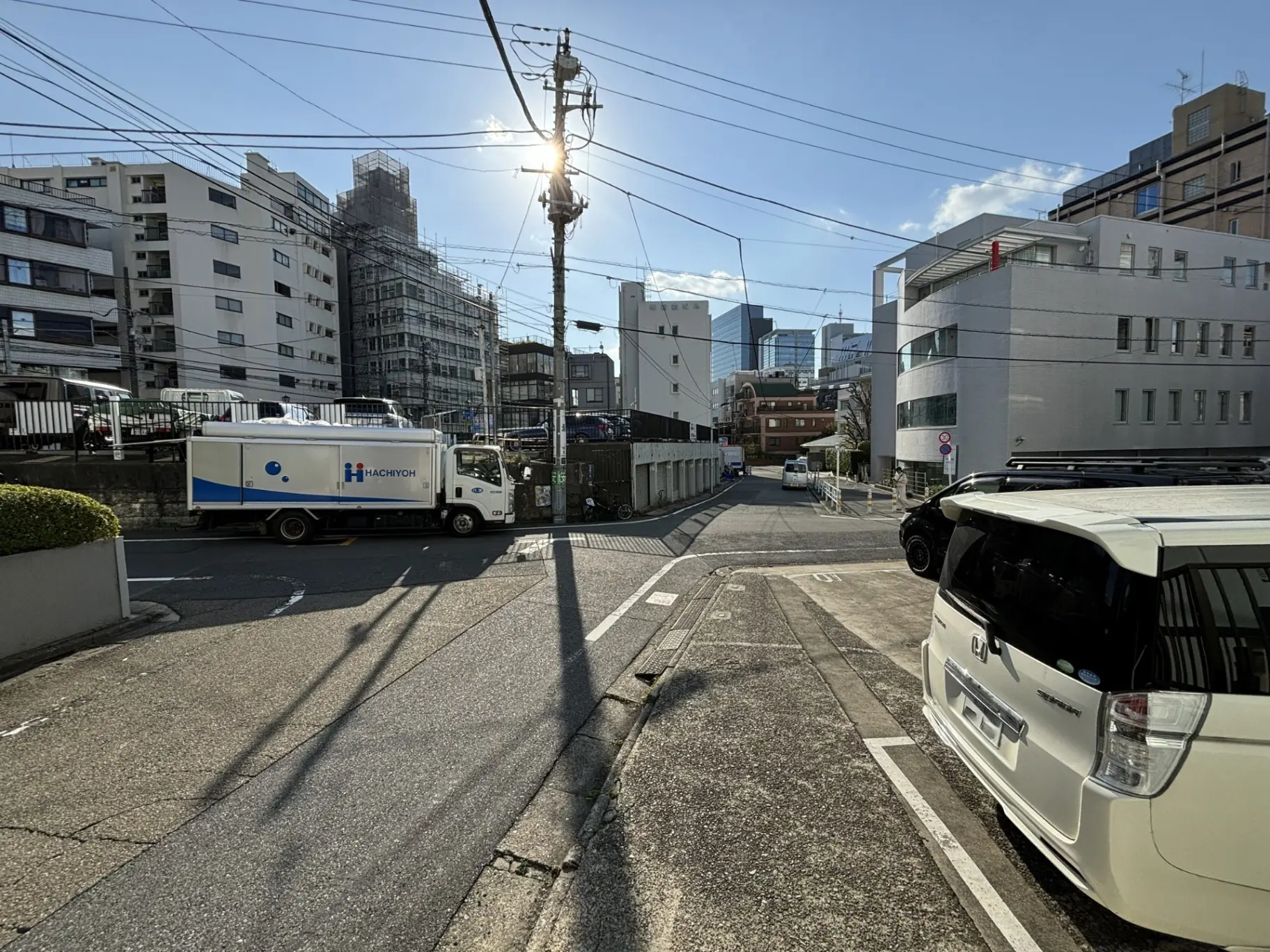 晴天の日本の市街地で撮影された写真、建築現場、移動式の事務所トラック、駐車された車、電柱と電線が見える風景