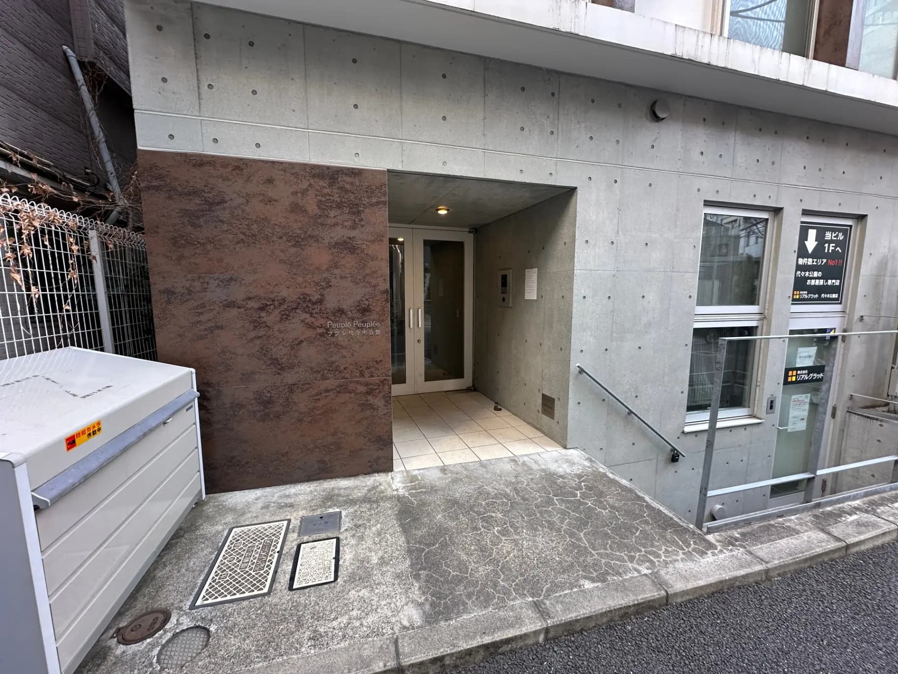 現代的なデザインのオフィスビルエントランス、コンクリート壁とガラス扉、案内看板が設置