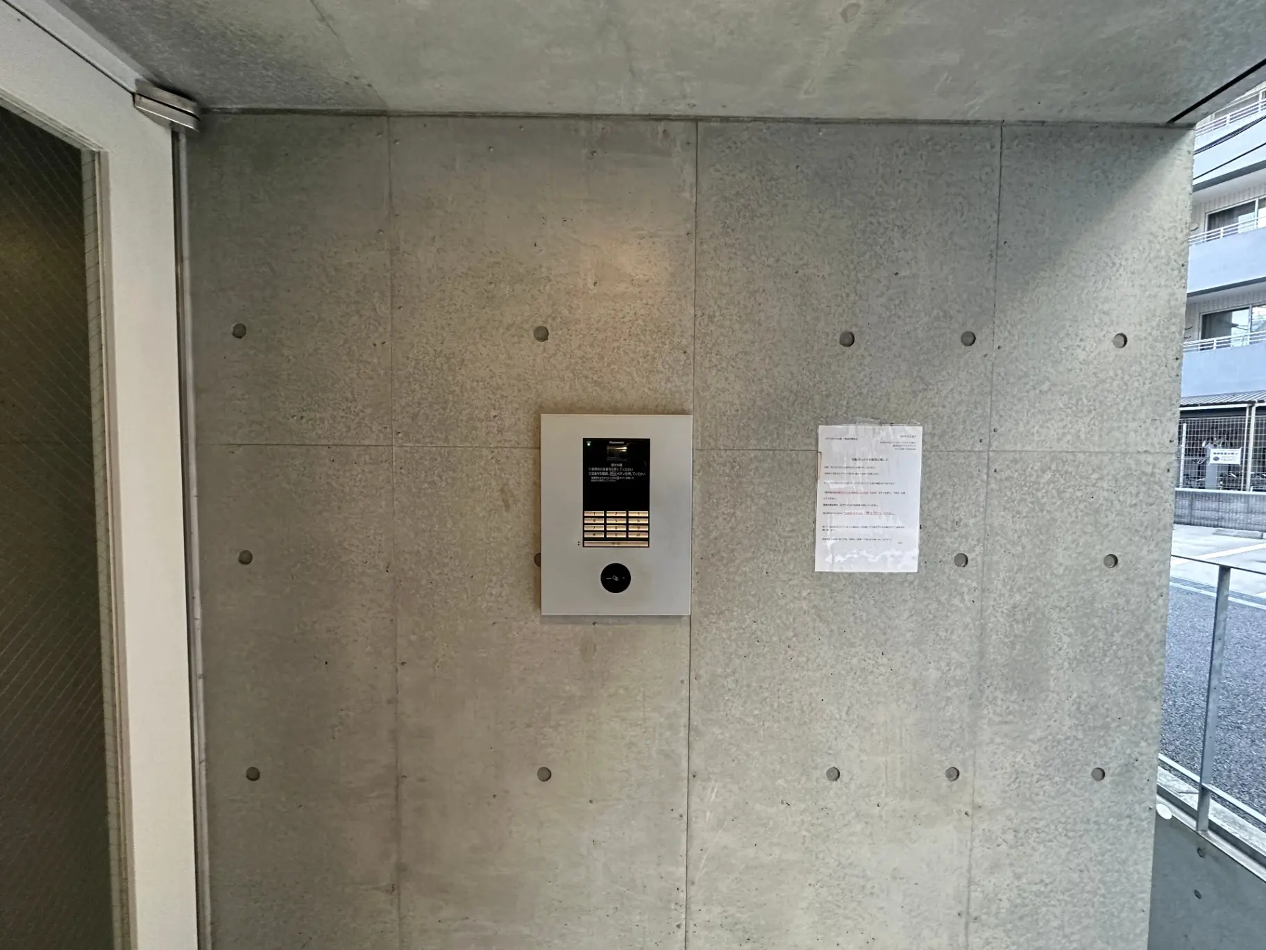 建物のエントランスに取り付けられたインターホンと掲示物、コンクリートの壁面