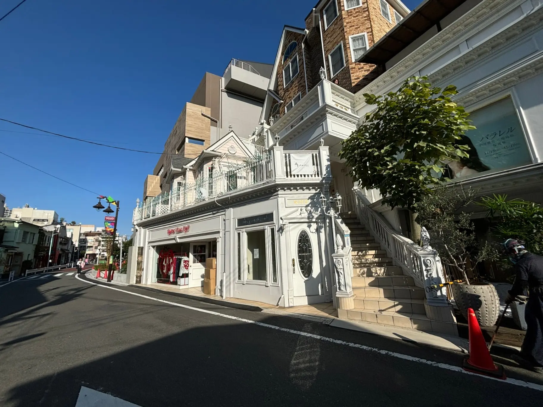 街角に建つクラシックな外観のビルと店舗、青空の下、歩行者と交通信号が見える風景