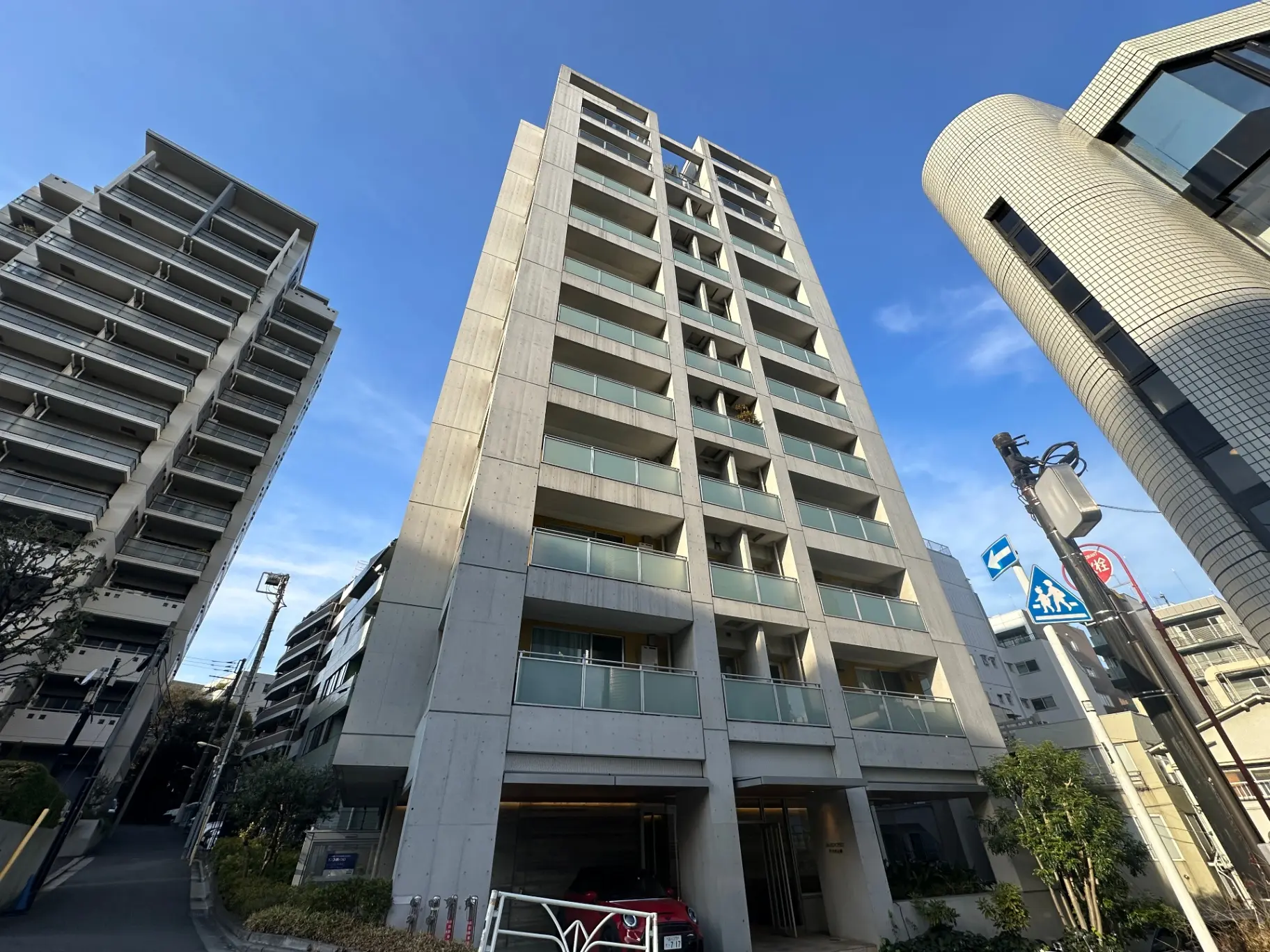 都市風景のマンション外観、現代的なデザインの建物、碧い空と緑の木、交通標識と街灯のある道路