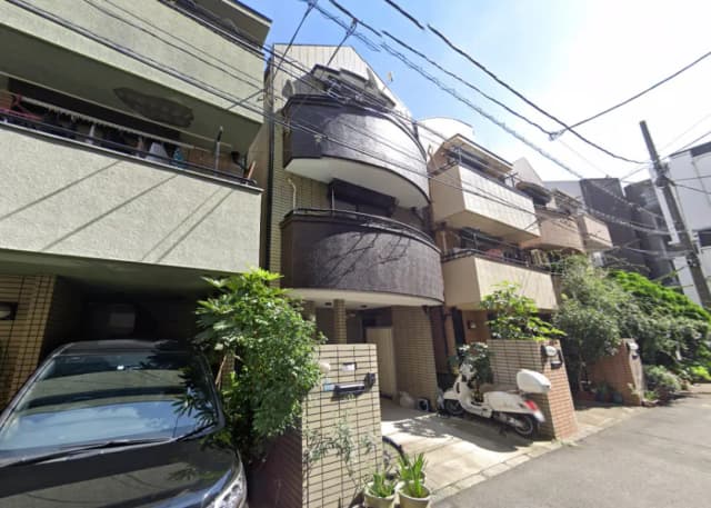 - モダンな外観の集合住宅、黒いバルコニーと緑豊かなエントランス、周囲に植栽と駐車場がある風景