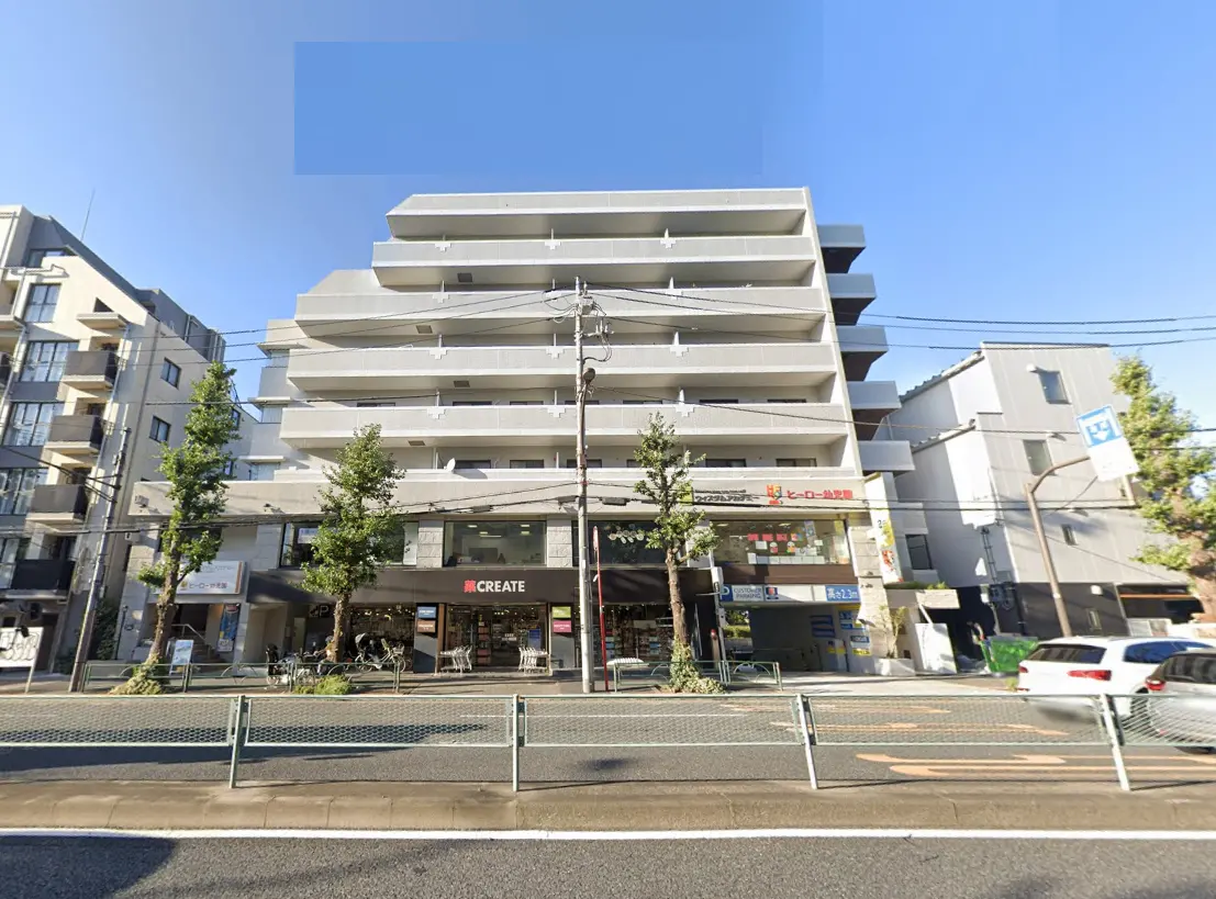 - 白い外壁のマンション、1階にはCREATEという店舗があり、周囲には緑の木々と道路が見える活気ある街並み
