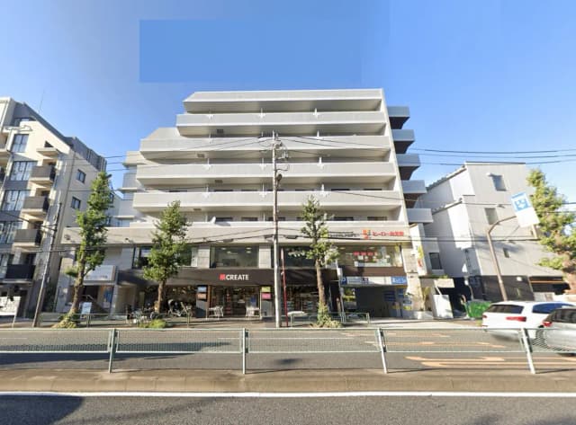 - 白い外壁のマンション、1階にはCREATEという店舗があり、周囲には緑の木々と道路が見える活気ある街並み