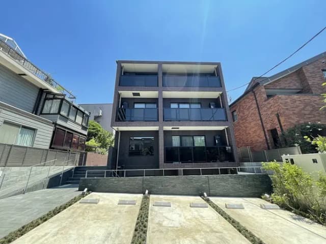 - 現代的な外観の三階建て住宅、広々としたバルコニーと大きな窓、周囲に緑の landscaping が整ったエリア