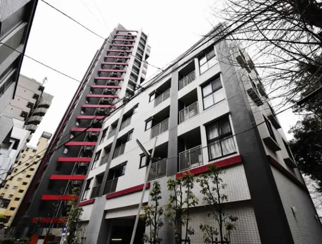 - モダンなデザインのマンション外観、白と黒のタイル張り、赤いアクセントを持つ高層ビルと周囲の樹木