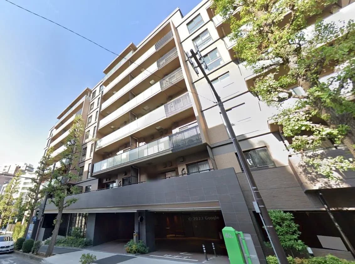現代的な外観の都市型マンション、ツリーが並ぶ歩道、地上階には駐車場入り口