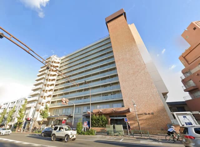 - 近代的な外観の高層マンション、道路沿いに立ち並ぶ車と街灯、青空に映えるデザイン