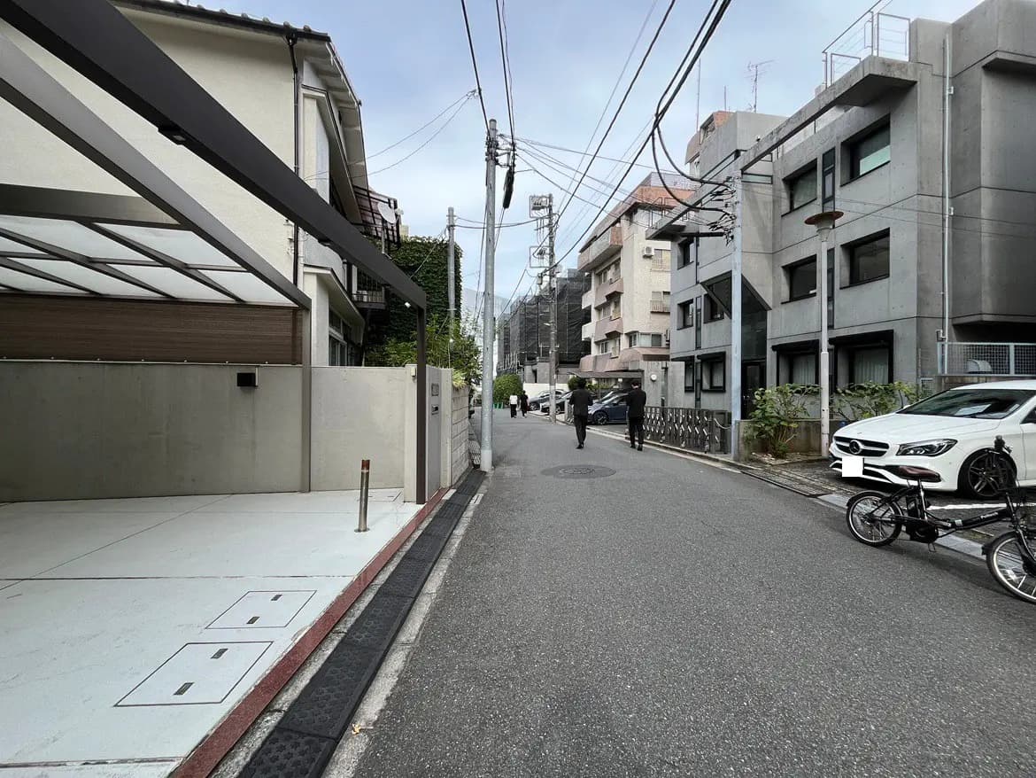 - コンクリートの外壁が特徴的な近代的な建物と駐車スペース、通りに歩く人々の姿も写った街並みの風景