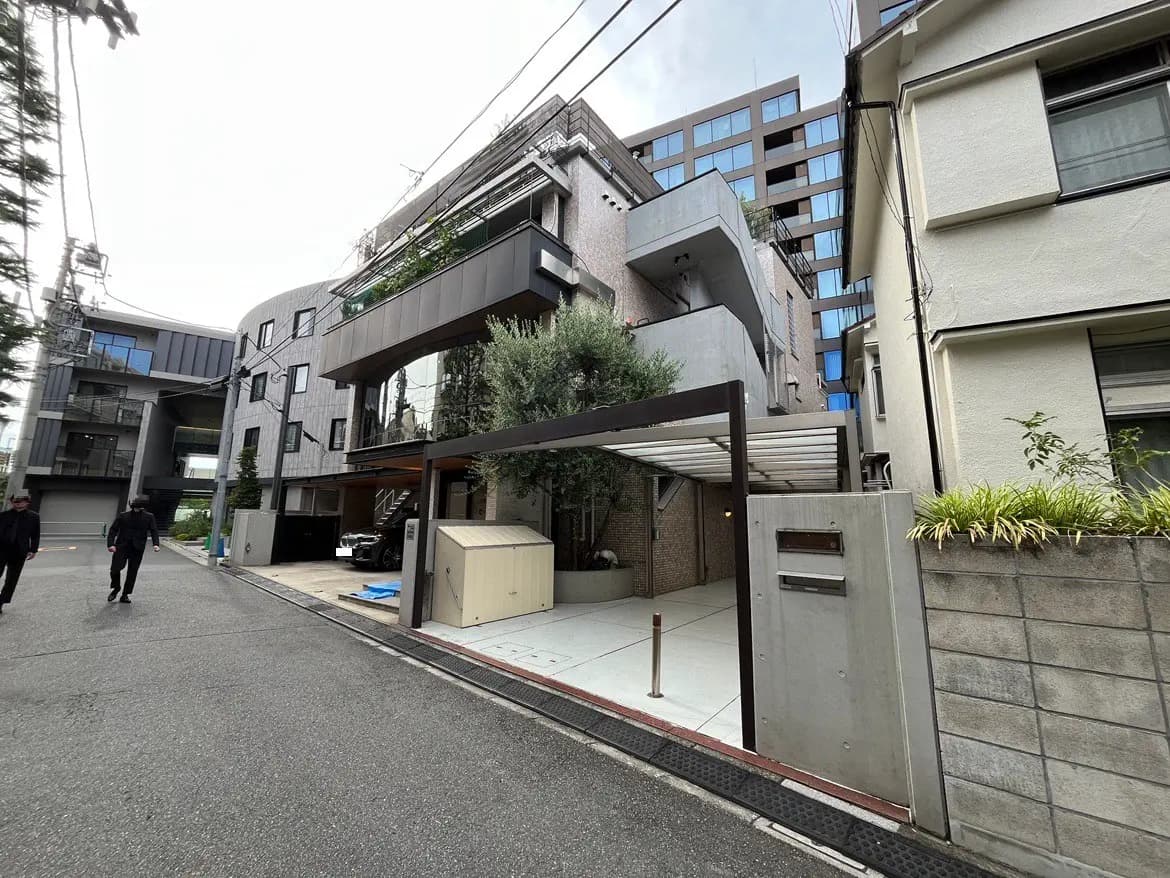 - モダンな外観の住宅、特徴的なデザインとガラスのバルコニー、周囲に緑がある街並みの風景