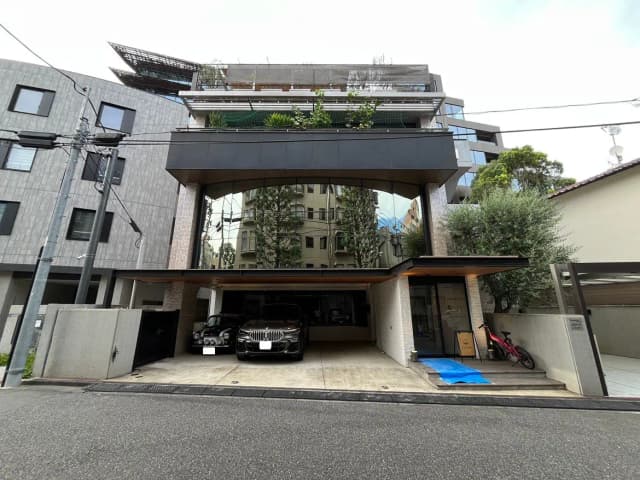 モダンなデザインの住宅外観、ガラス張りのファサード、駐車場には3台の車、周囲に緑の植栽があるエントランスエリア