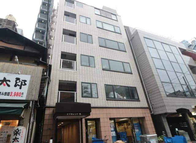都市のビル街に位置するモダンな外観のオフィスビルと周辺の商店、曇り空の日に撮影