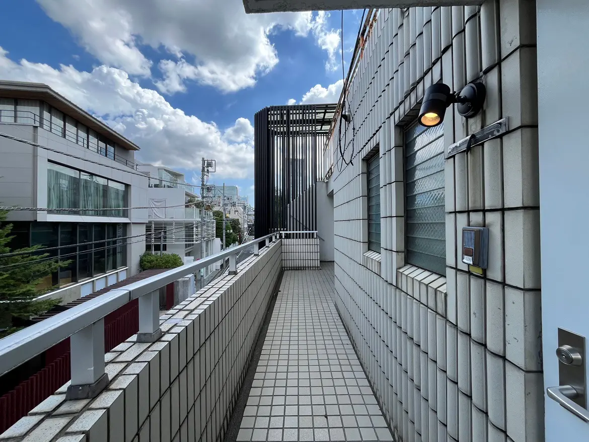 - 明るい空と雲が広がる中庭の通路、タイル張りの床と隣接する建物がある風景