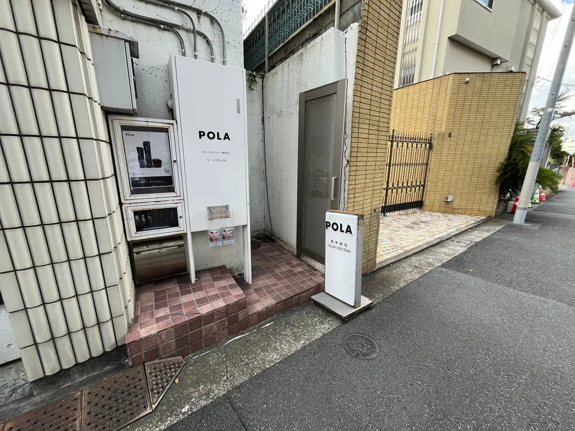 - POLAの店舗入口、白い看板と自動販売機が配置された歩道沿いの風景、周囲の建物が写っている
