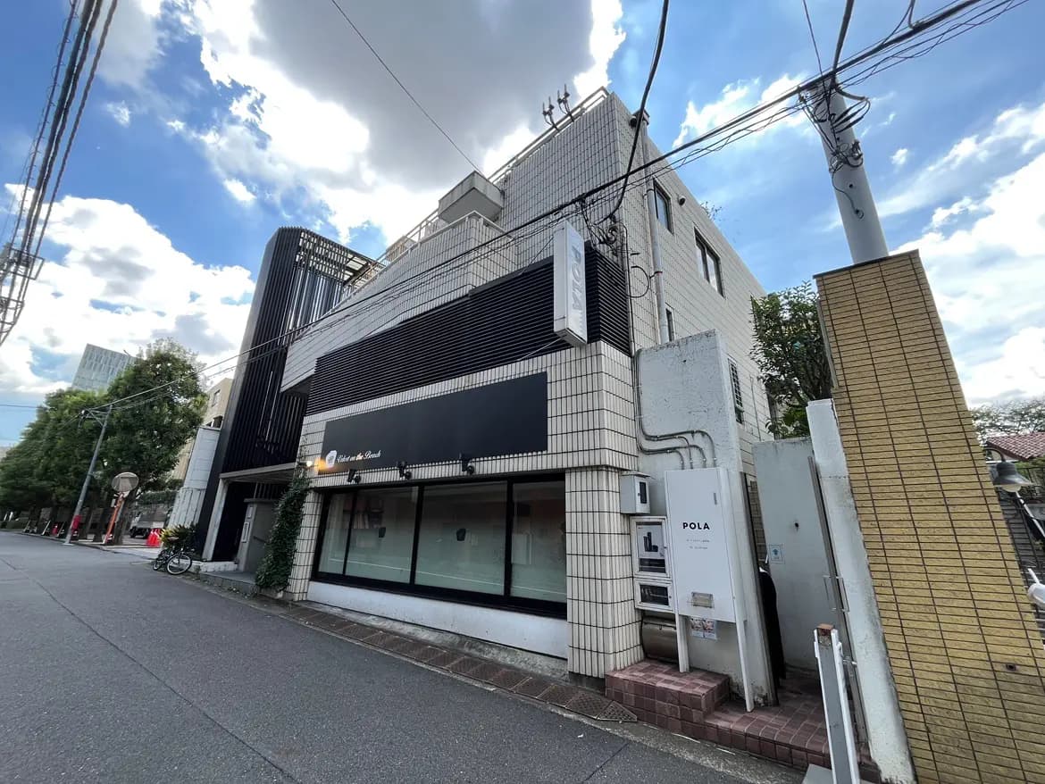 - 現代的な外観のビル、一階にはPOLAの看板が掲げられ、周囲には緑が見える街並みの風景