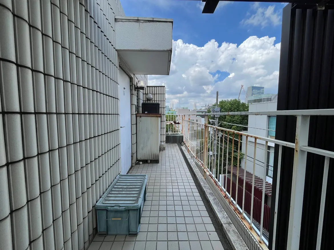 - 清潔感のあるバルコニー、タイル張りの床に青い収納ボックス、広がる青空と白い雲が映えるシンプルなデザイン