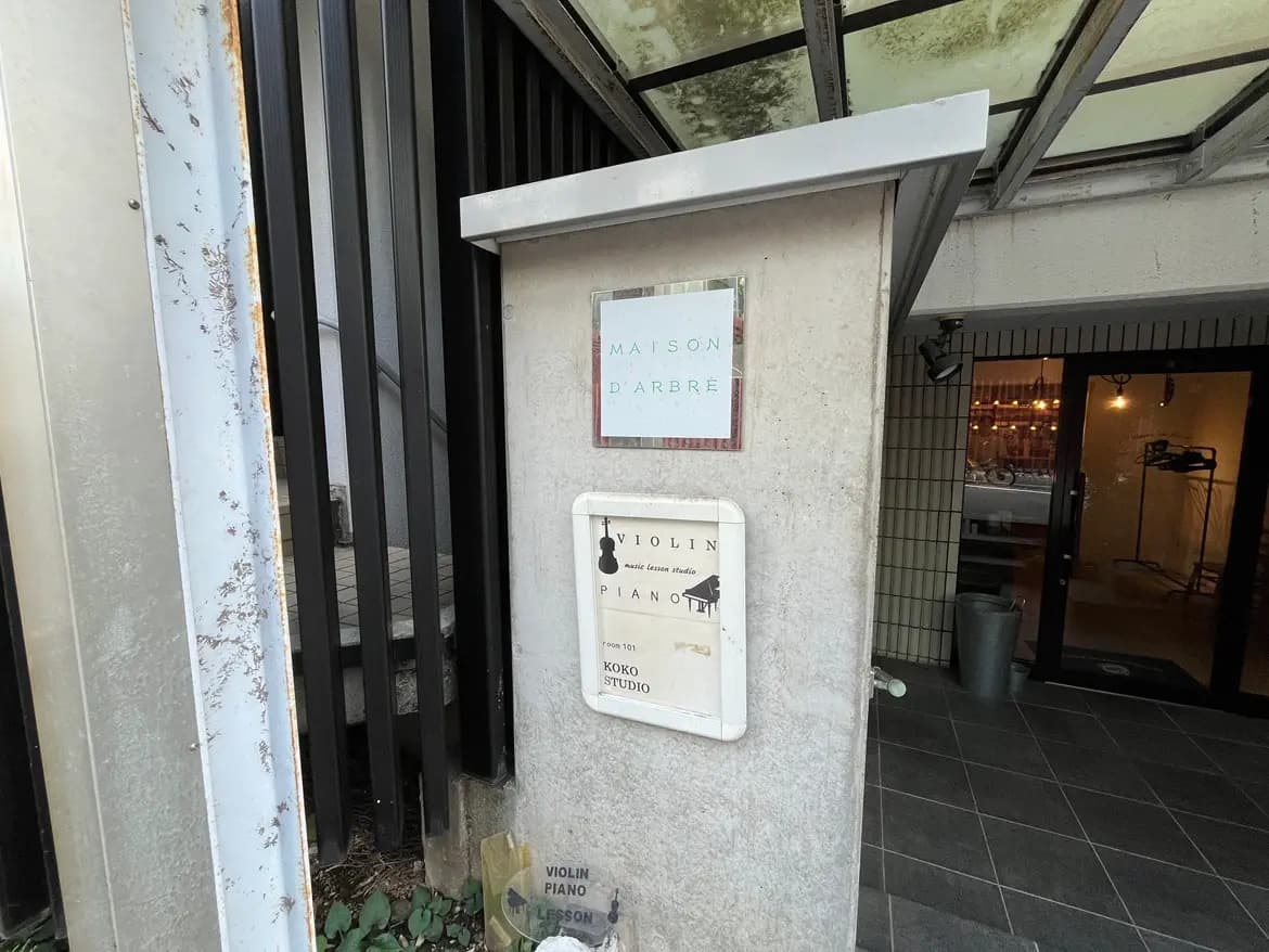 - 音楽教室の入口、ピアノとバイオリンのレッスンを提供するスタジオの看板が掲げられたコンクリートの柱と周囲の環境