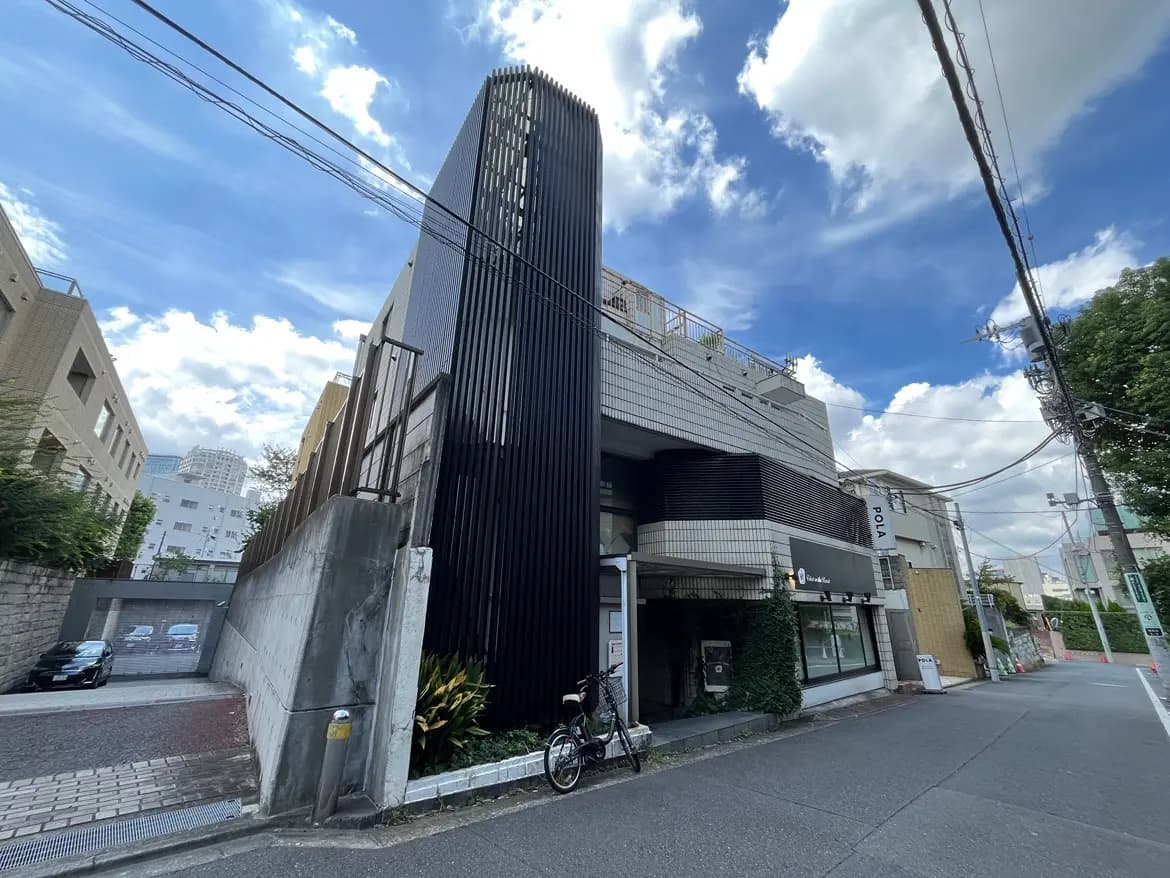 - モダンな外観の建物、黒い縦格子のファサードと白いタイルの部分、青空と雲が広がる街の風景