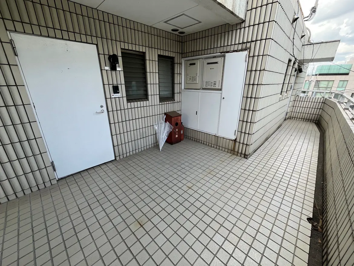 - コンクリートタイルの広いバルコニー、白いドアと郵便受け、傘が置かれたエントランスエリア