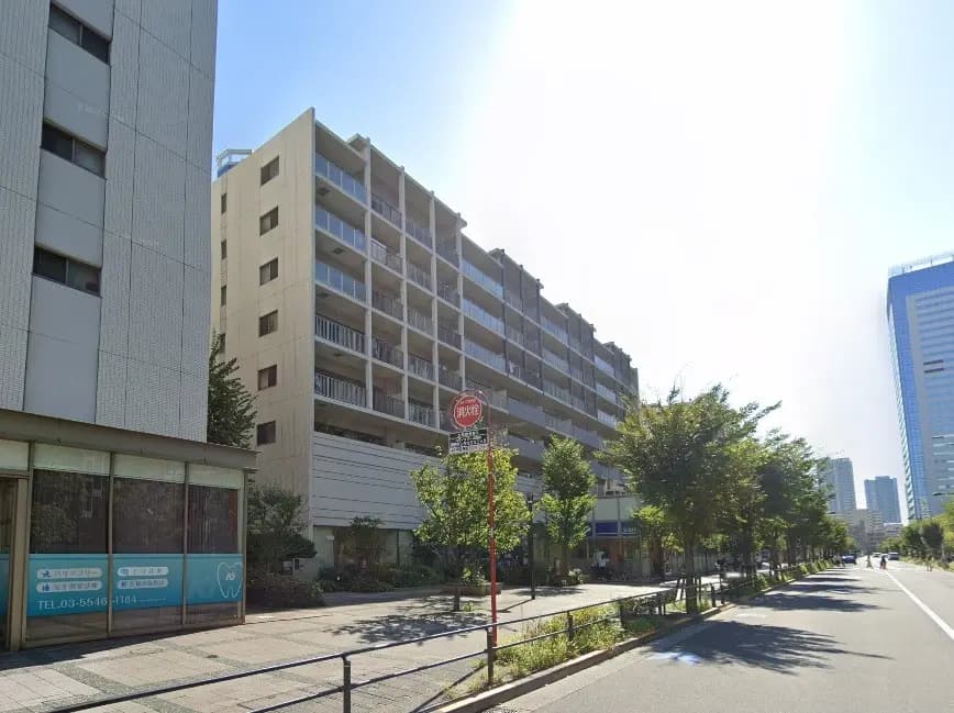都市の通りにあるマンションの外観、晴れた日の青空、歩道と緑の木