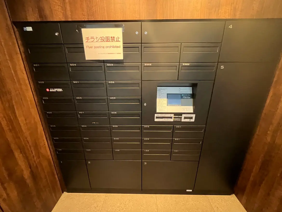 マンションの入り口にある宅配ボックスと郵便受け、注意書きの表示がある現代的な配達システム