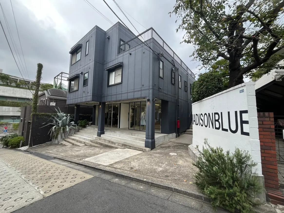 モダンな外観のビル "MADISONBLUE" の入り口、都会的なデザインと緑の植物が印象的なストリートビュー