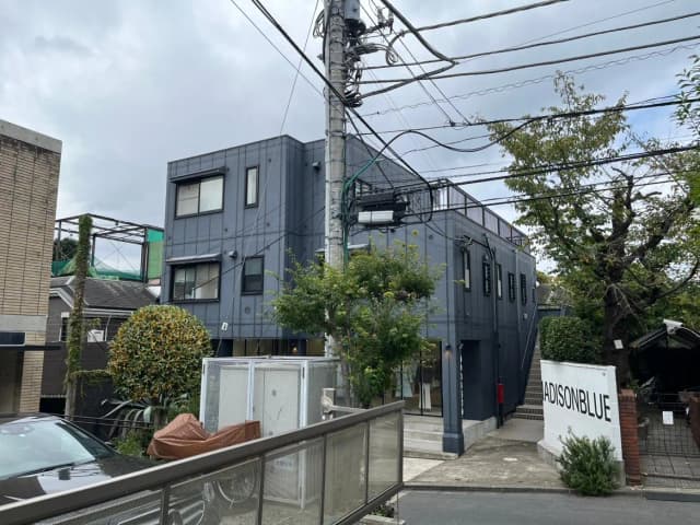 現代的な外観の建物と入口、樹木に囲まれた風景、電線が交差する都市の景観