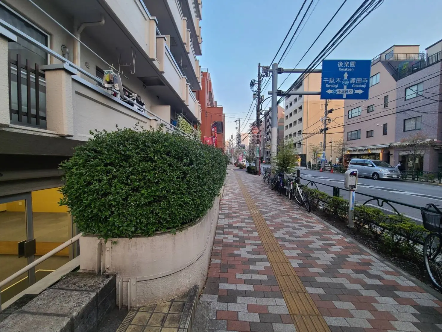 日本の静かな住宅街の歩道、緑の植物と自転車駐輪場、道路標識と薄暮の空