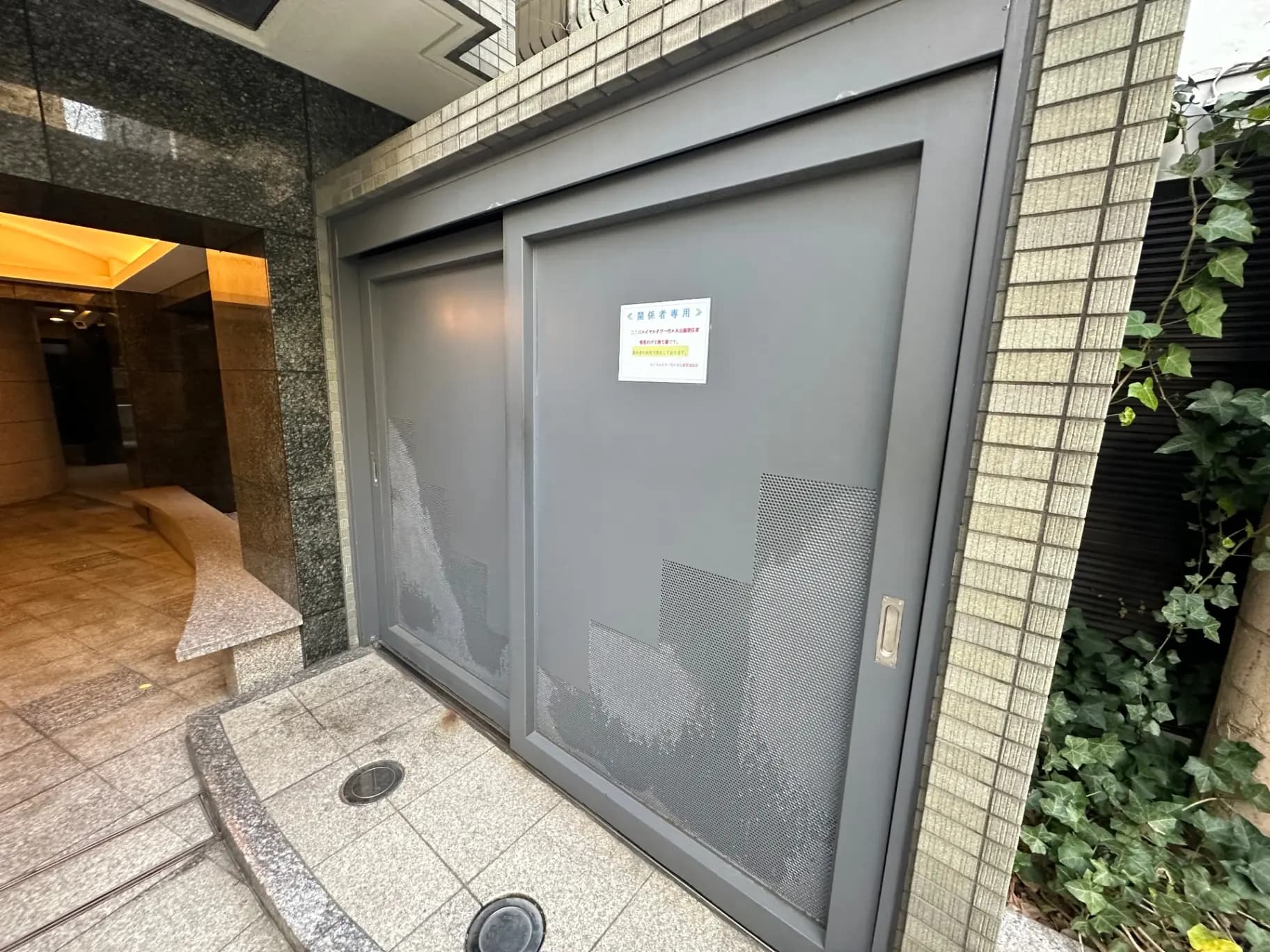 現代的なデザインのビルの入口、グレーの扉と黒御影石の外装、緑の植物がある外観