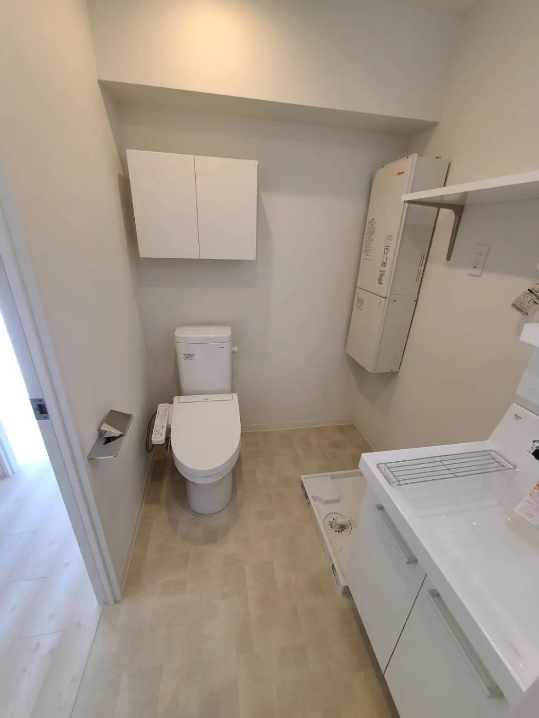 清潔感ある白い壁のトイレと洗濯機のある洗面所、木目調のフローリングと明るい照明のインテリア