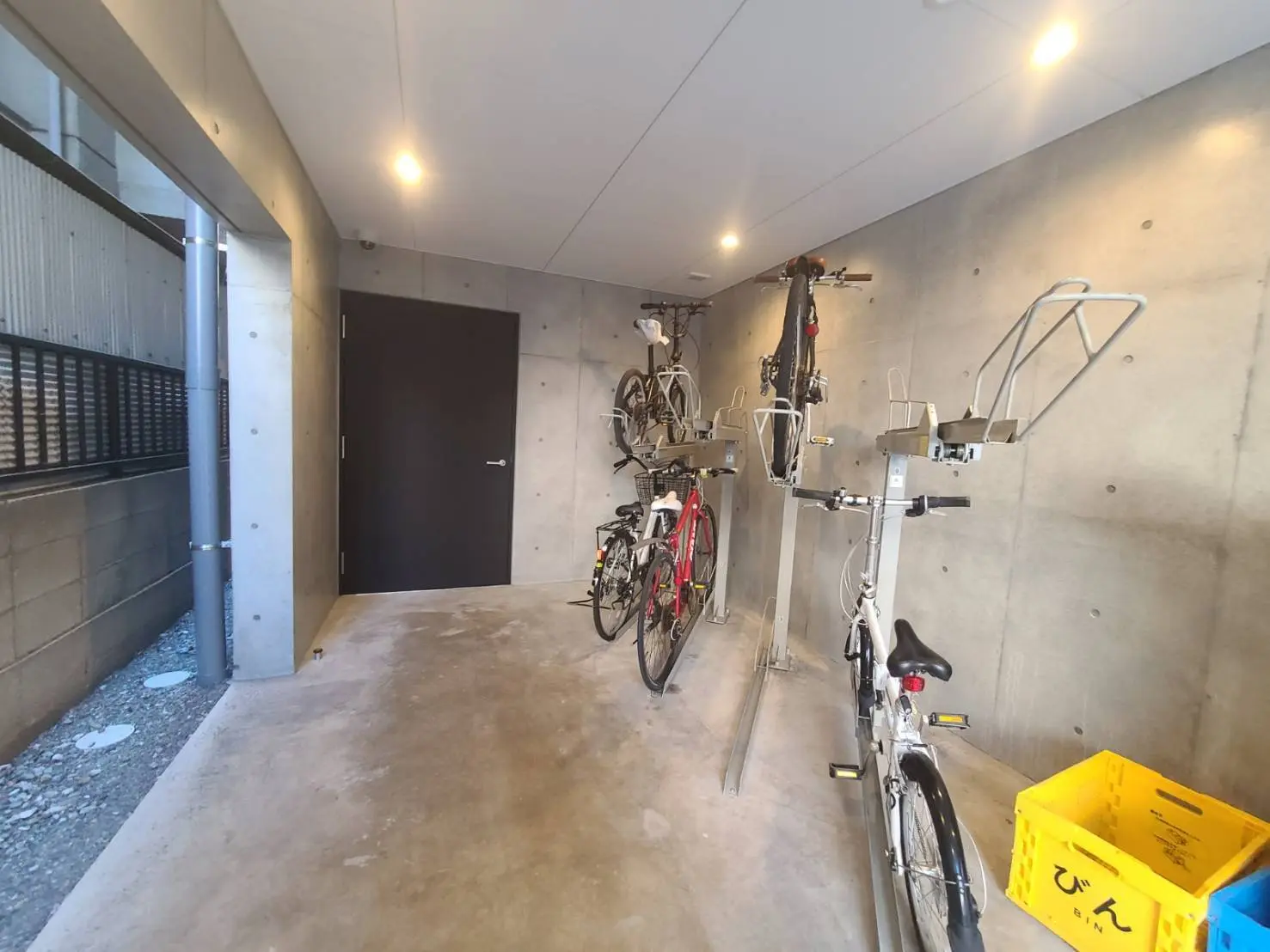 コンクリート壁のモダンな自転車駐輪場、壁掛け式のスタンドに吊るされた複数の自転車、クリーンで広々とした空間