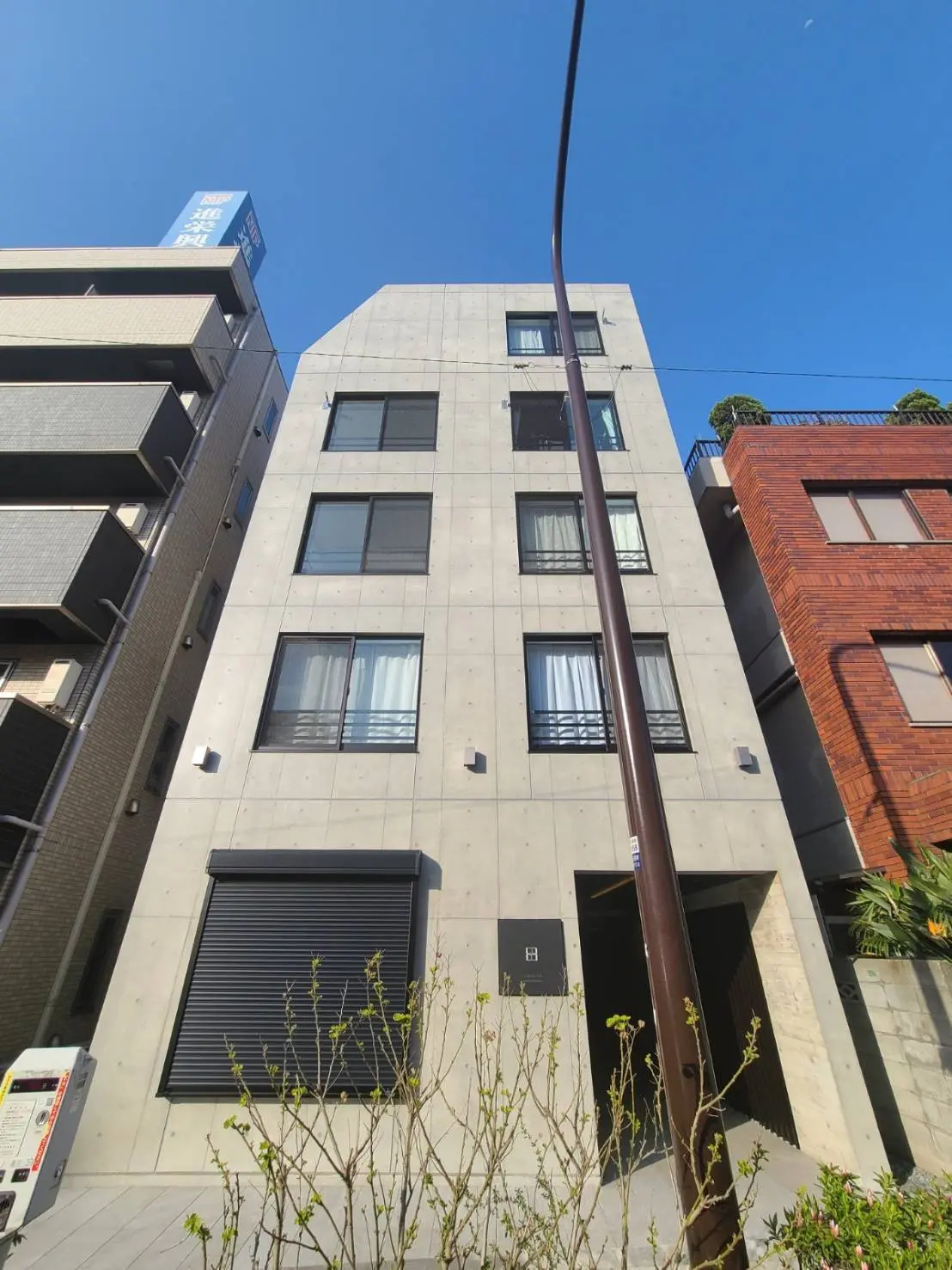 モダンな外観の都市型マンションビル、青空の下での清潔感あふれる外壁とシャッター付きの窓